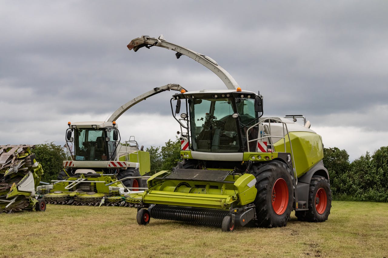 Two modern combine harvesters parked on a farm field under cloudy skies.