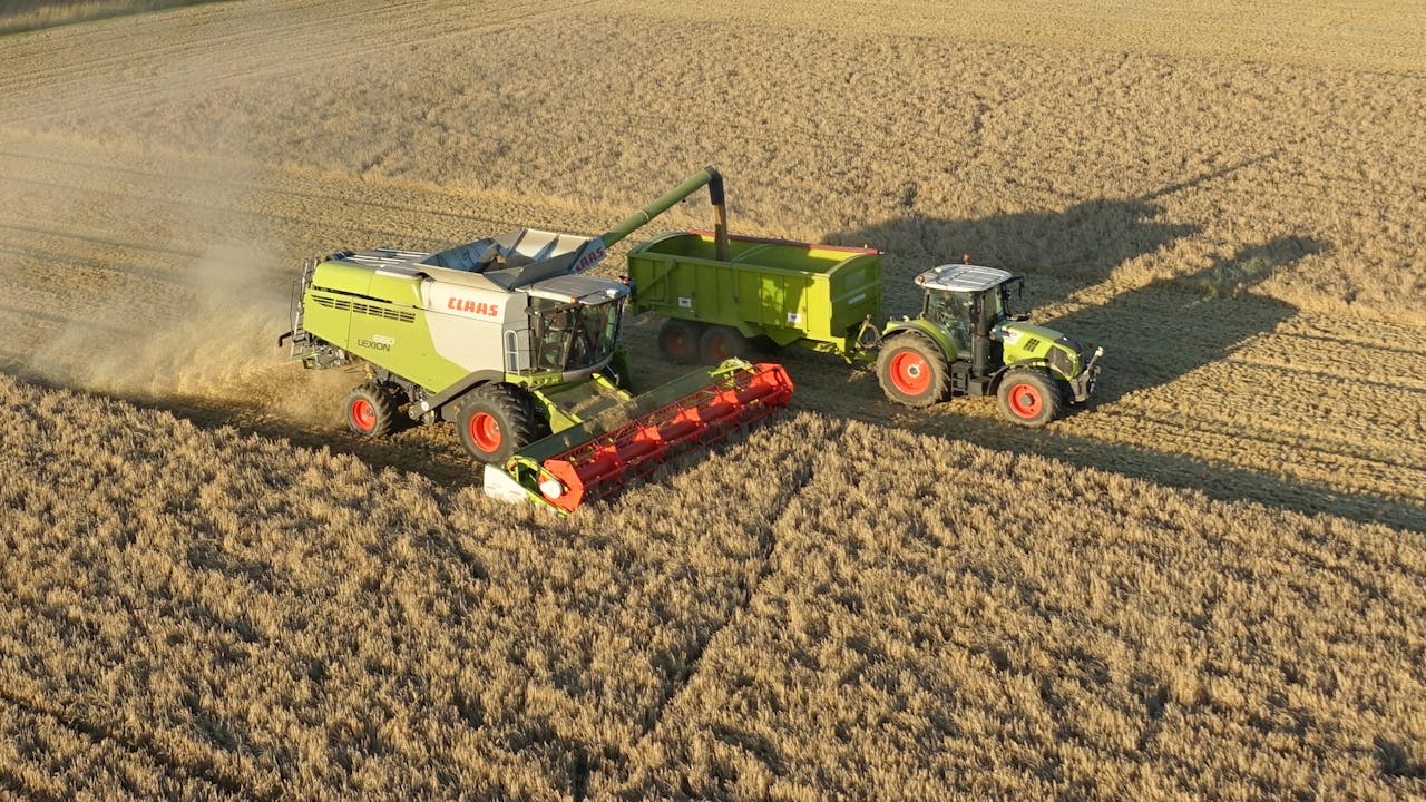Aerial shot capturing a combine harvester and tractor working in a golden wheat field.