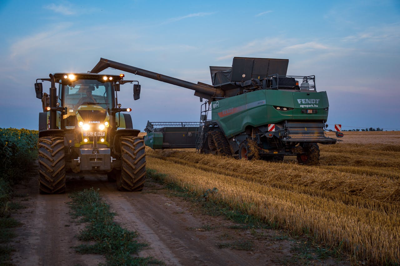Tractor and harvester working in a field at dusk, showcasing rural agriculture machinery.